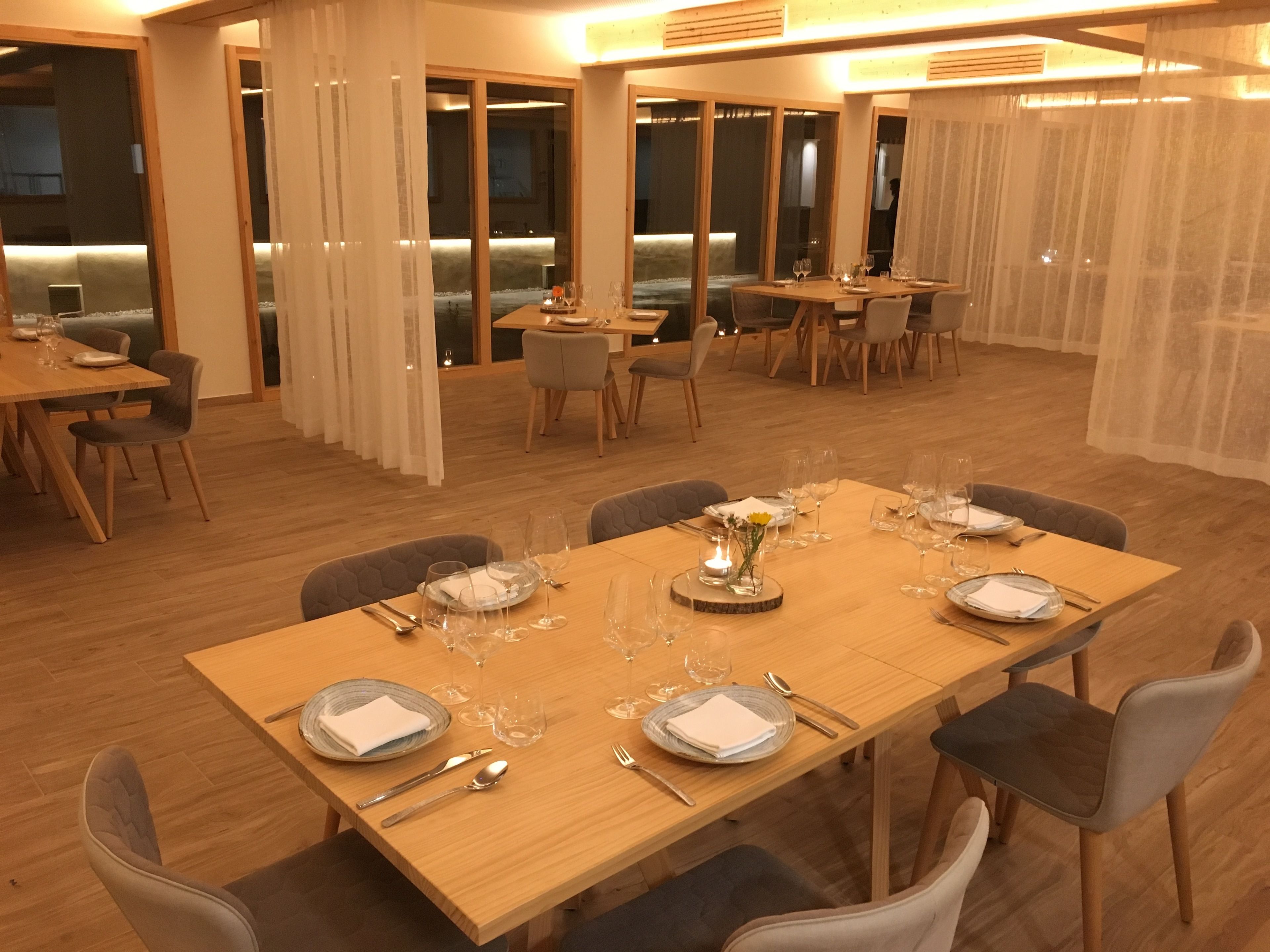 A spacious dining area with multiple tables set for dining, featuring wooden flooring and modern furniture.