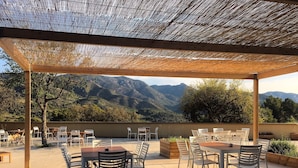 An outdoor patio with tables and chairs, a pergola, and a mountainous backdrop.