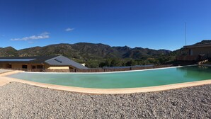 A swimming pool with a mountain backdrop, a building with a sloped roof, and a fence.