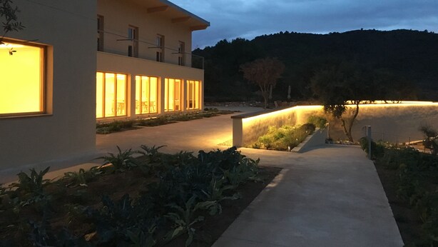 A modern building with large windows and a well-lit pathway leading to a landscaped area.