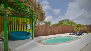 A pool area with a blue inflatable pool, lounge chairs, and a wooden fence. - Pista Q (Oranjestad)