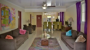 A spacious living room with two sofas, a coffee table, and a colorful rug. There is a dining area in the background with chairs and a table. - Pista Q (Oranjestad)