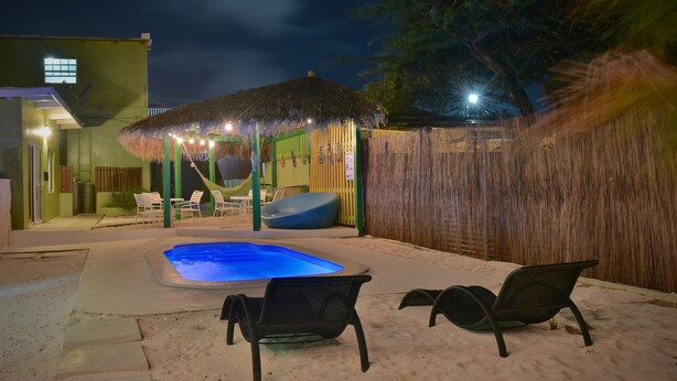 A backyard with a swimming pool, lounge chairs, and a thatched-roof gazebo. - Pista Q (Oranjestad)