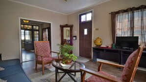 A living room with a sofa, two patterned chairs, a round glass table with a plant, a television, and a globe on a cabinet. - Pista Q (Oranjestad)