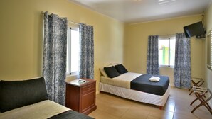 A bedroom with two beds, a TV mounted on the wall, and a desk with a chair. - Pista Q (Oranjestad)