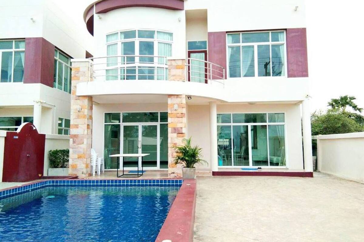 Une maison moderne à deux étages, dotée d’une piscine, de grandes fenêtres et d’un balcon.