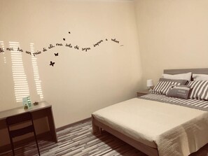 A bedroom with a bed, bedside tables, and a wall with a decorative phrase and butterfly decals. - Le Querce di Mamre (Assisi)