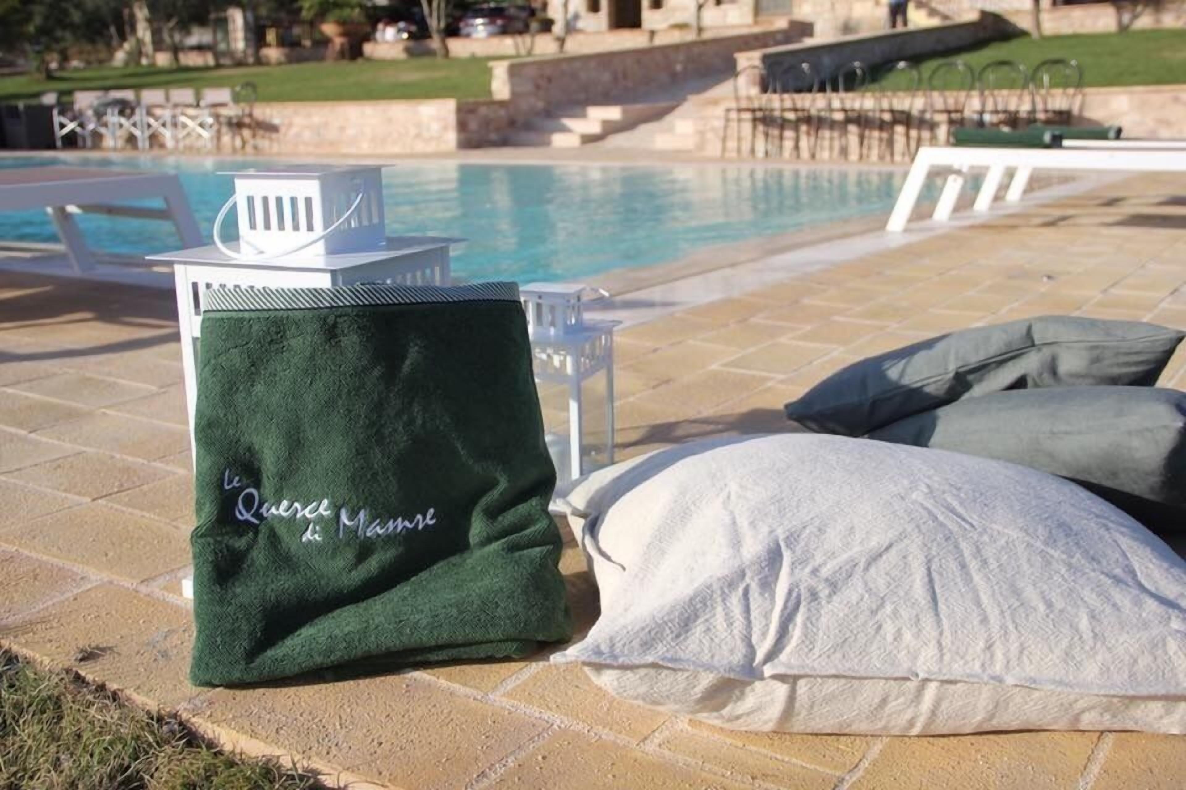 Ein Poolbereich mit einer grünen Strandtasche, weißen Kissen und einem weißen Stuhl.