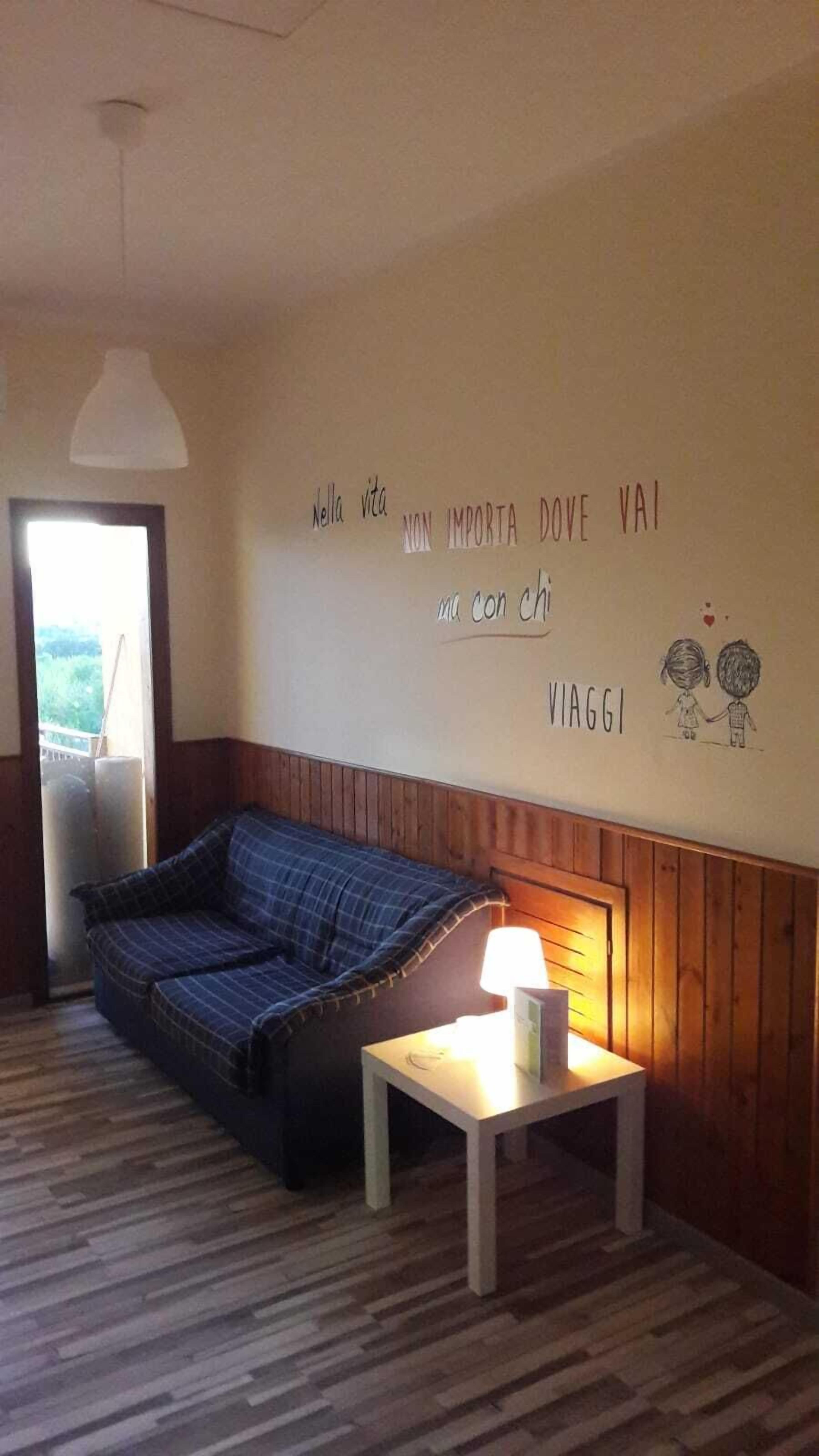 A cozy room with a blue sofa, a small table with a lamp, and a wall with a motivational quote and a drawing of two people holding hands.