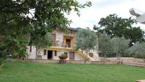 Un edificio de piedra con un balcón amarillo, rodeado por un patio cubierto de césped y árboles.