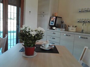 A modern kitchen with a coffee machine, a potted plant, and a dining area with a table and chairs. - Le Querce di Mamre (Assisi)