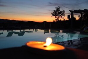 A serene outdoor pool area at dusk with a lit candle, lounge chairs, and a pergola. - Le Querce di Mamre (Assisi)