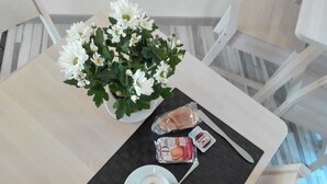 Una mesa con un arreglo floral blanco, un plato con una taza de café y alimentos envasados.