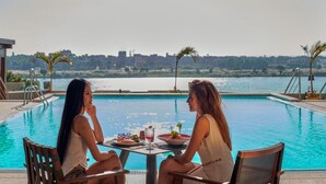 Two people dining at a table by a pool with a city view. - Holiday Inn Cairo Maadi (Cairo)