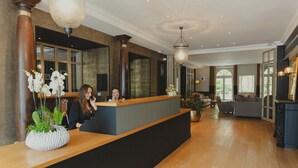 A reception area with a wooden reception desk, a large potted plant, and a seating area with sofas and a fireplace. - Hôtel Le d'Avaugour (Dinan)