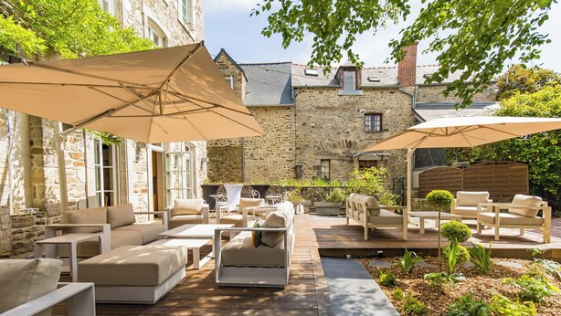 A patio with outdoor furniture and umbrellas, surrounded by stone walls and greenery. - Hôtel Le d'Avaugour (Dinan)