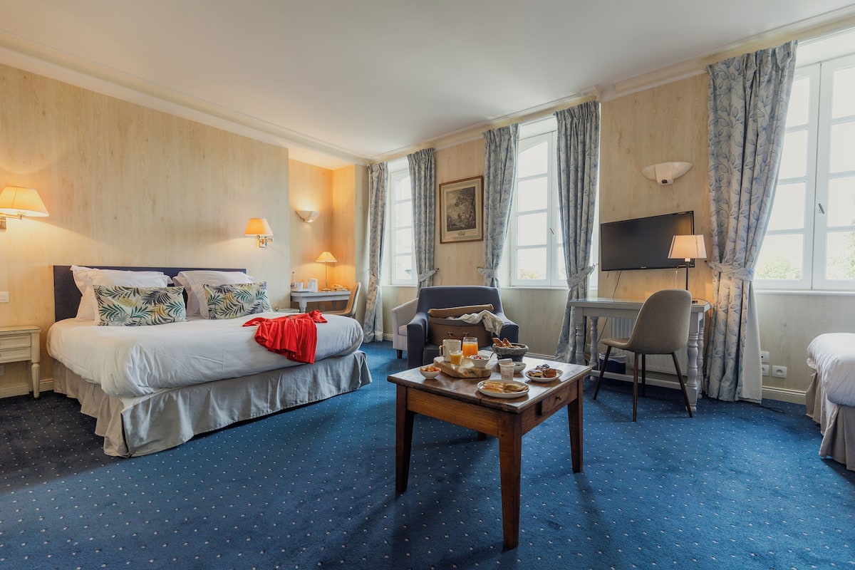 A hotel room with a bed, a desk with breakfast, a chair, and a TV.
