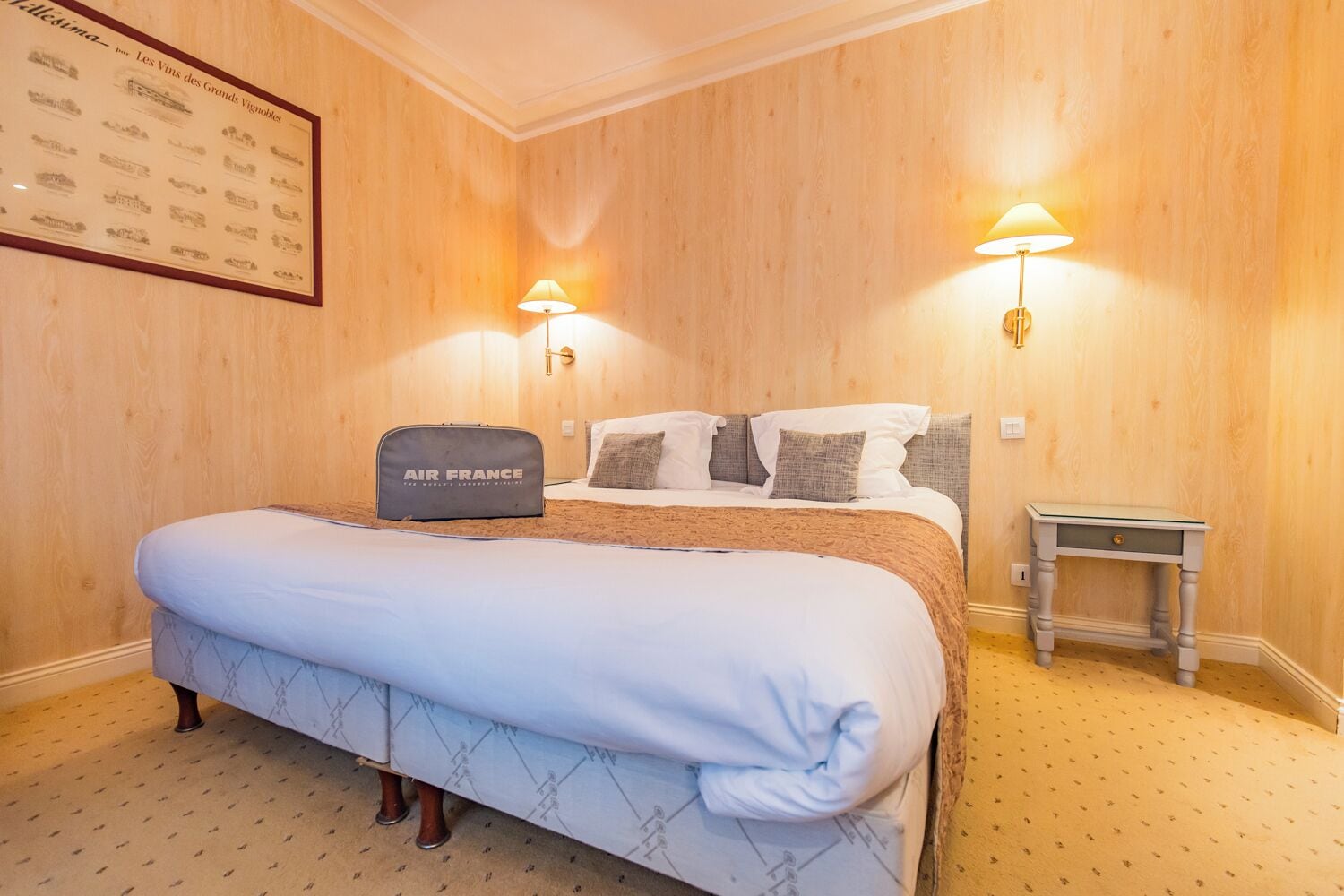 Habitació d'hotel amb un llit gran, dues làmpades al costat del llit, una taula de nit petita i un quadre amb marc a la paret.
