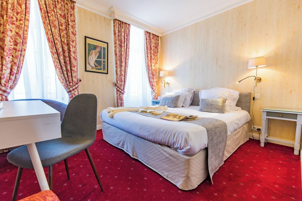 A hotel room with a bed, a desk, a chair, and a lamp.