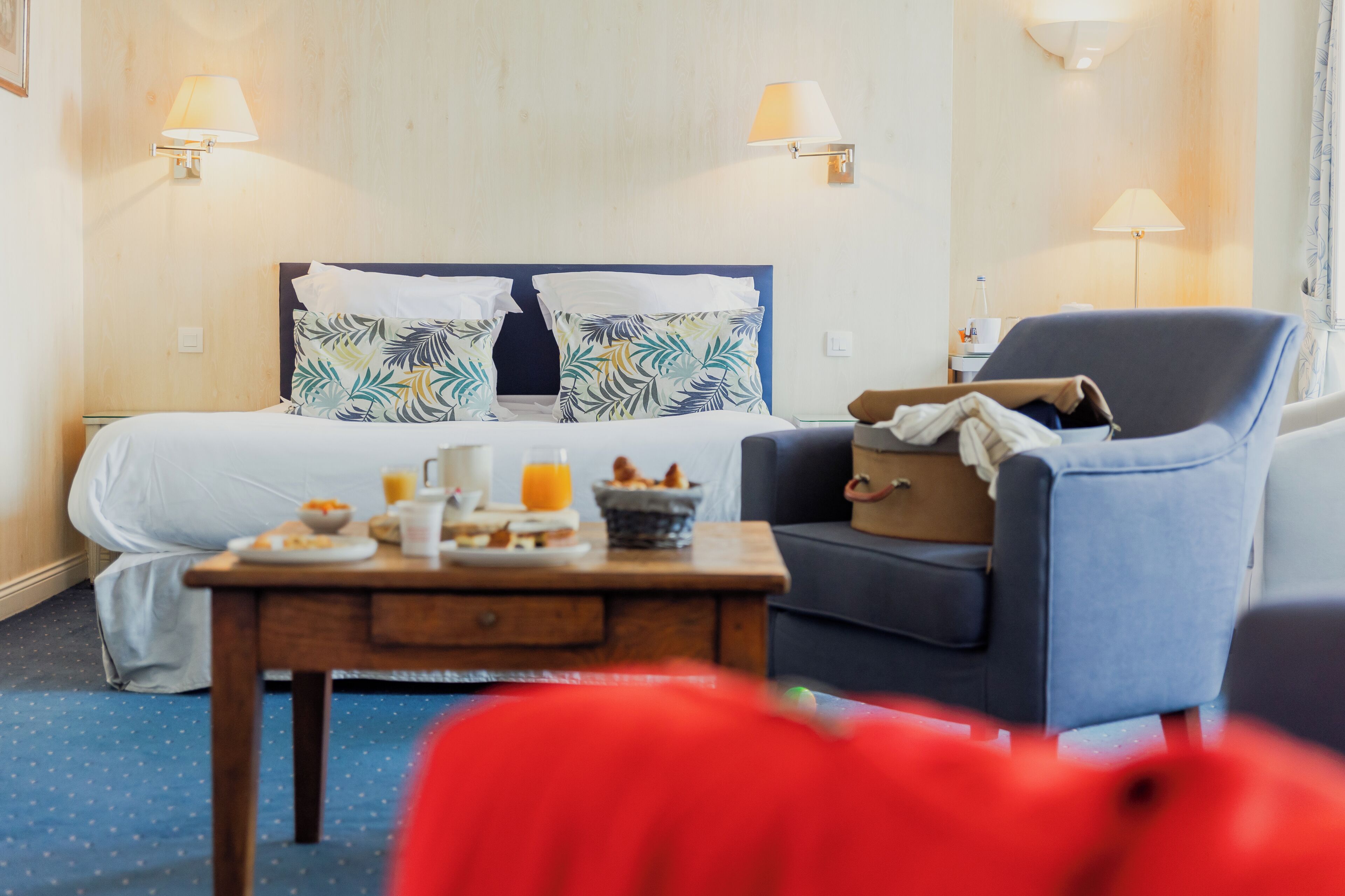 Een hotelkamer met een bed, een stoel, een tafel met ontbijtartikelen en wandlampen.