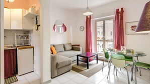 A compact living space with a kitchenette, a sofa, a dining table with chairs, and a window with curtains. - Attico Sannio 2 (Rome)