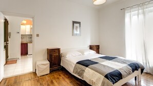A bedroom with a bed, wooden nightstands, a bedside table, a hanging light fixture, a door leading to a bathroom, and a window with sheer curtains. - Attico Sannio 2 (Rome)