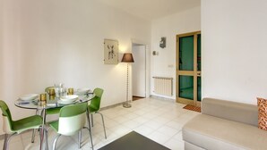 A modern living room with a glass dining table, green chairs, a beige sofa, and a floor lamp. - Attico Sannio 2 (Rome)