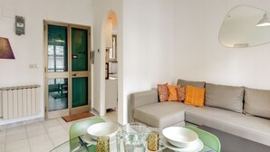A modern living room with a sofa, a dining table with bowls and glasses, and a glass door leading to another room. - Attico Sannio 2 (Rome)