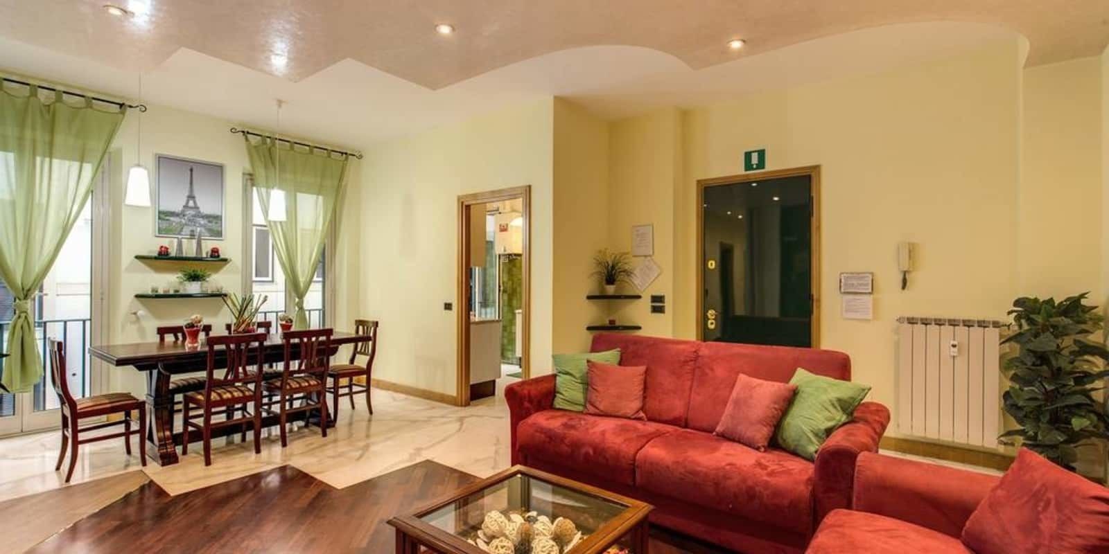 A living room with a red sofa, a glass coffee table, and a dining area with a wooden table and chairs.