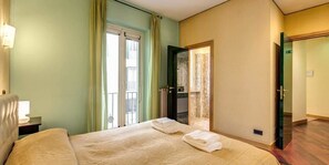 Une chambre d’hôtel avec un lit, une table de chevet, une fenêtre avec des rideaux et une porte donnant sur une autre pièce.