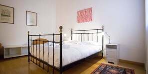 Ein Einzelbett mit Metallgestell, ein Nachttisch, eine Wandlampe und ein gemustertes Teppich.