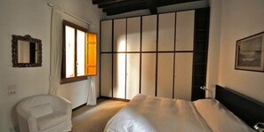 Un dormitorio con cama, una silla, un armario y una ventana.