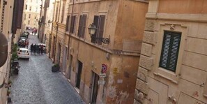 Una estrecha calle adoquinada flanqueada por edificios históricos con ventanas con contraventanas y un cartel de prohibido estacionar.