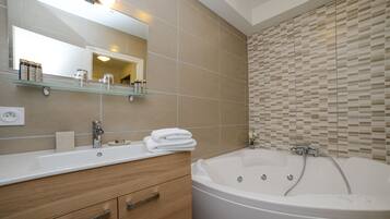 A modern bathroom with a large bathtub, a glass shelf with toiletries, and a wooden vanity.