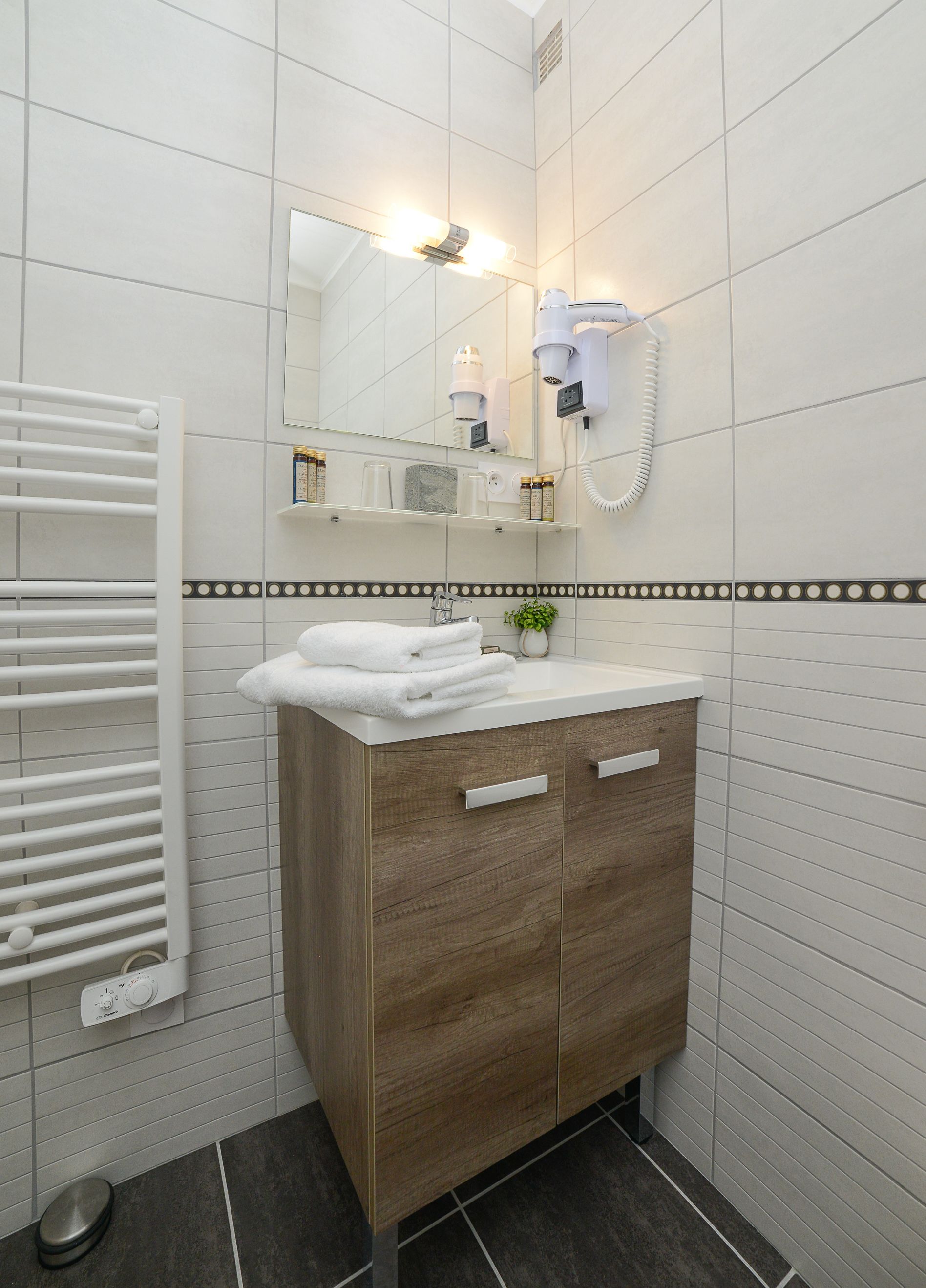 Un baño con tocador de madera, toallero, espejo y secador de pelo fijado a la pared.