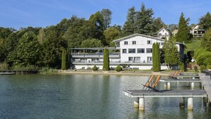 A lakeside hotel with a white exterior, multiple balconies, and a dock with lounge chairs. - Hôtel Restaurant Novalaise Plage (Novalaise)