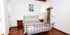 A bedroom with a metal bed frame, a bedside table with a lamp, a radiator, and a door with a mirror. - Spanish Step Suite (Rome)