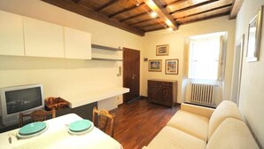 Un salon comprenant un canapé, un téléviseur, une table à manger avec des chaises, un plancher en bois et une porte donnant sur une autre pièce.