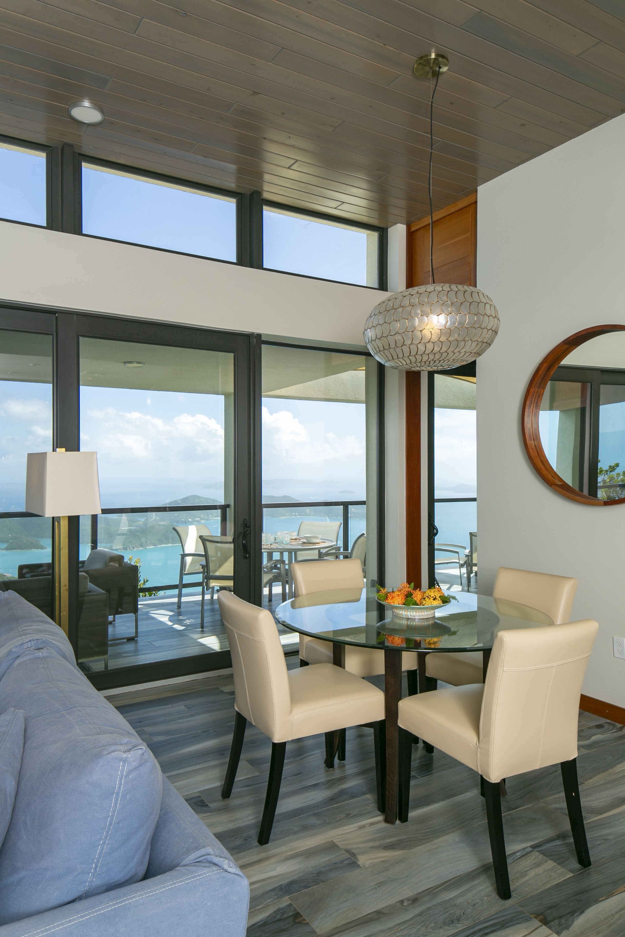 A modern dining area with a glass table, beige chairs, and a decorative light fixture.