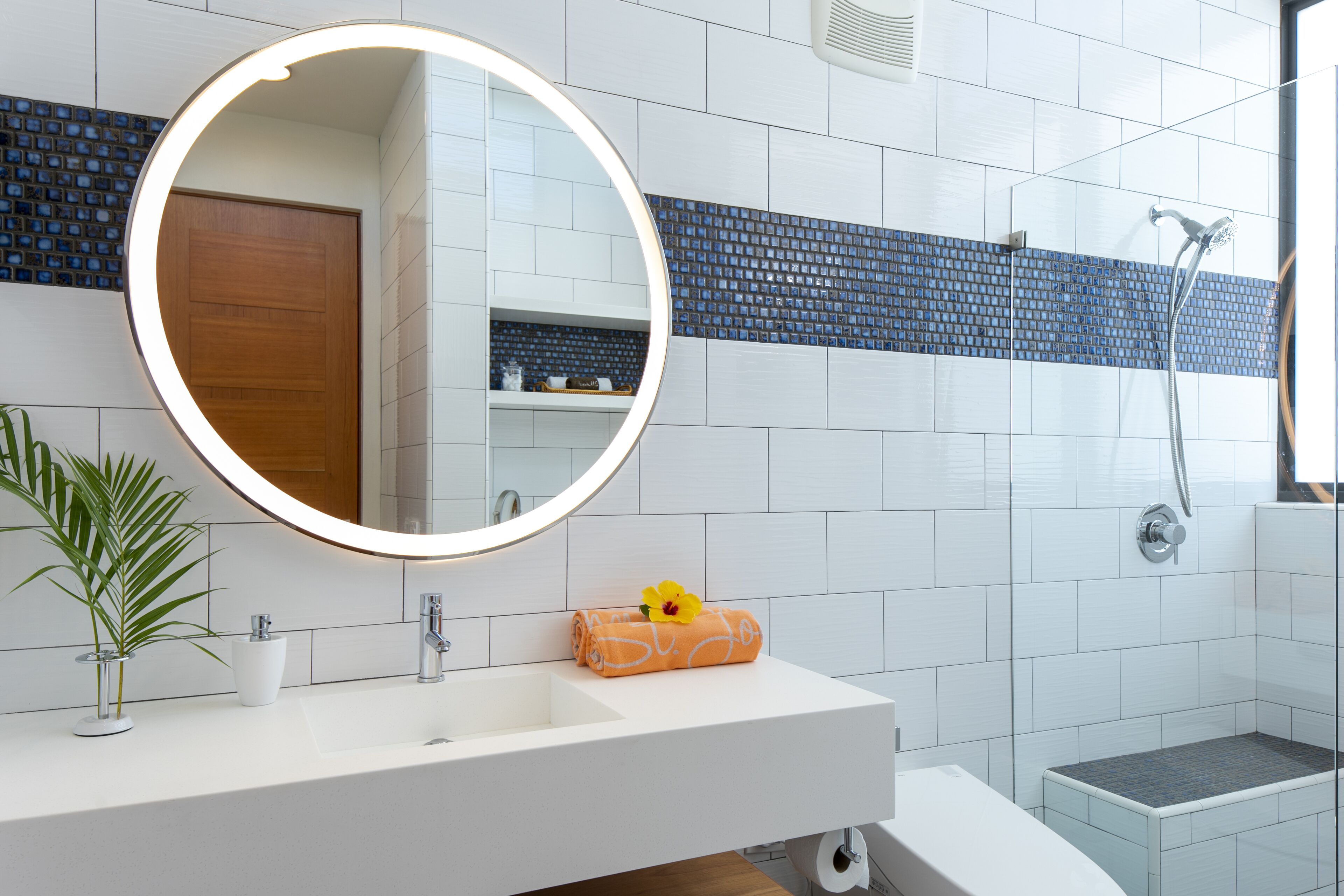 Een moderne badkamer met een witte wastafel, een ronde spiegel, een handdoek met een gele bloem, en een douchecel.