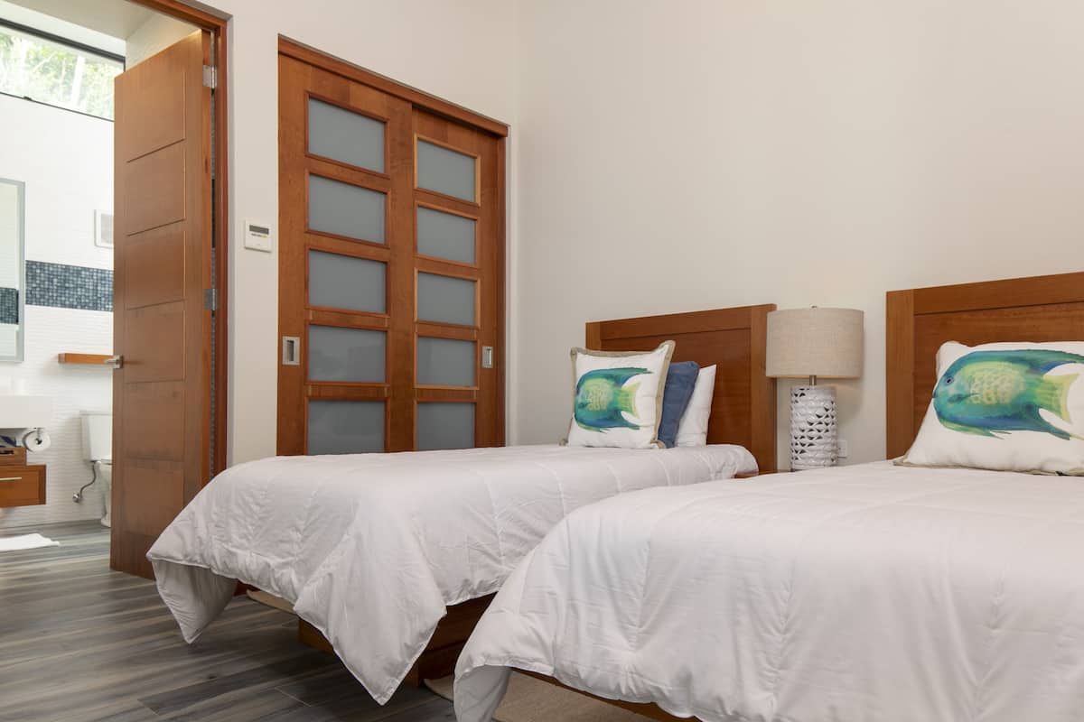 A hotel room with two beds, wooden headboards, white bedding, and a large window.