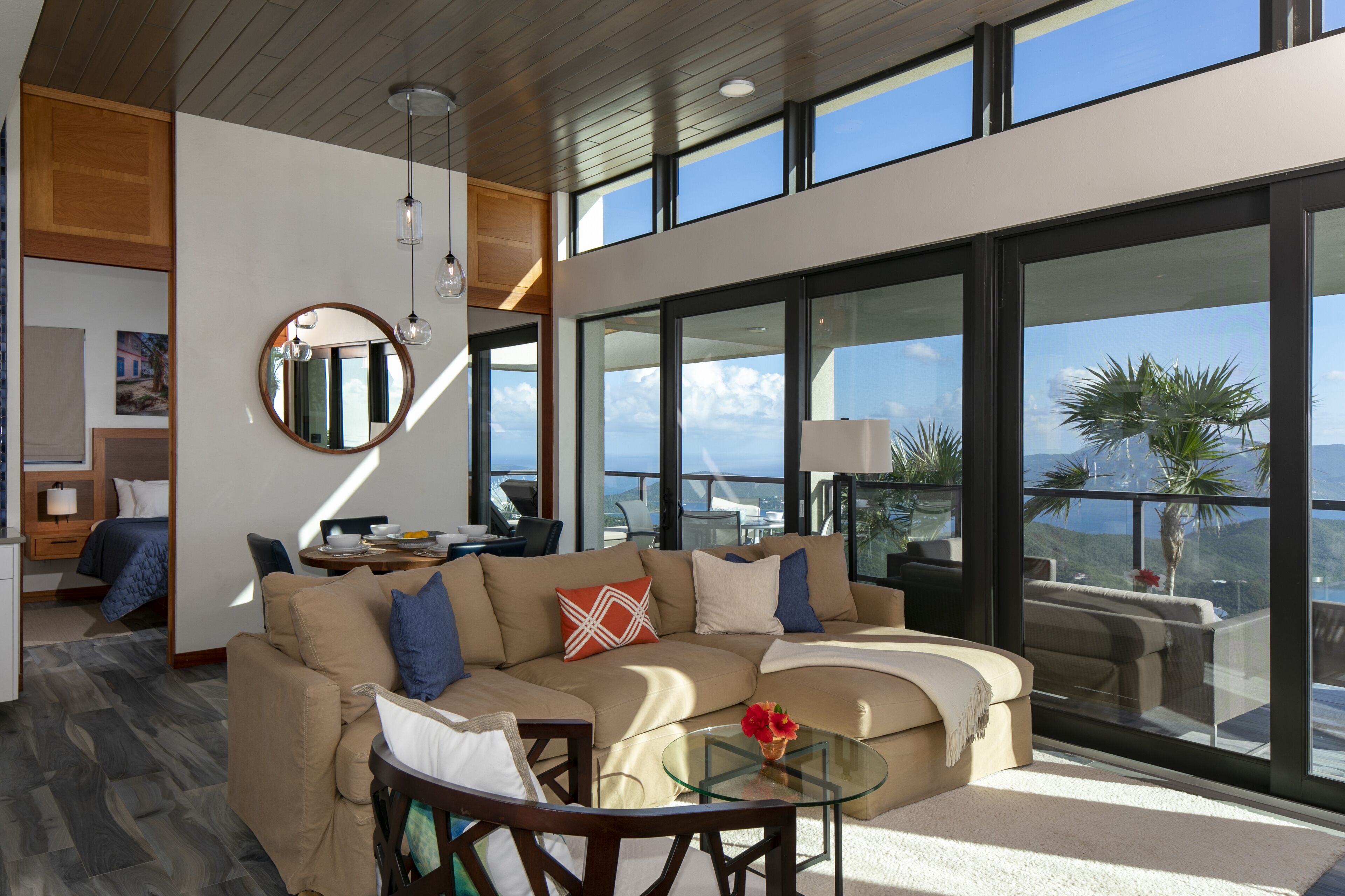 A modern living room with a large sectional sofa, a glass coffee table, and a view of the ocean through large windows.