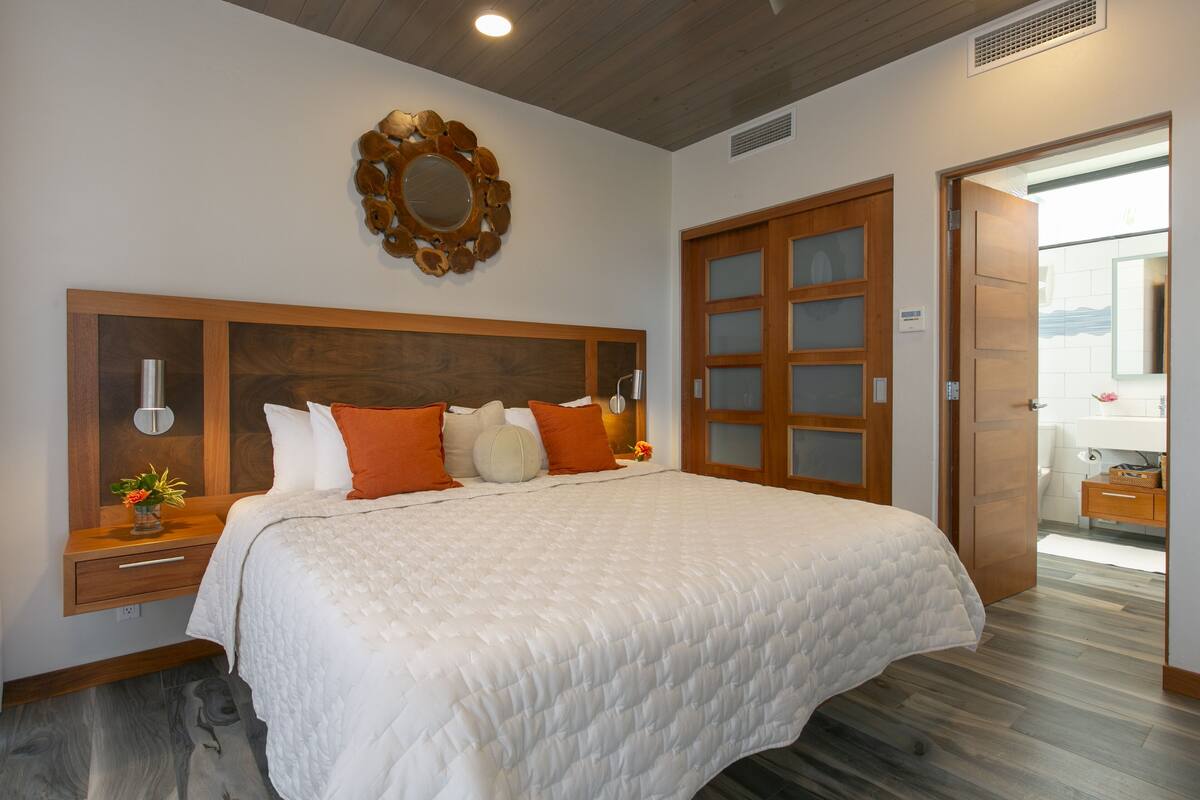 A neatly made bed with a wooden headboard, a bedside table with a lamp, and a mirror above the bed.