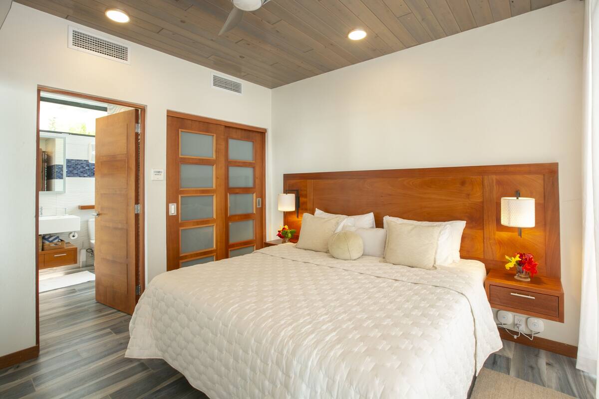 A bedroom with a large bed, wooden headboard, bedside lamps, and a nightstand with flowers.