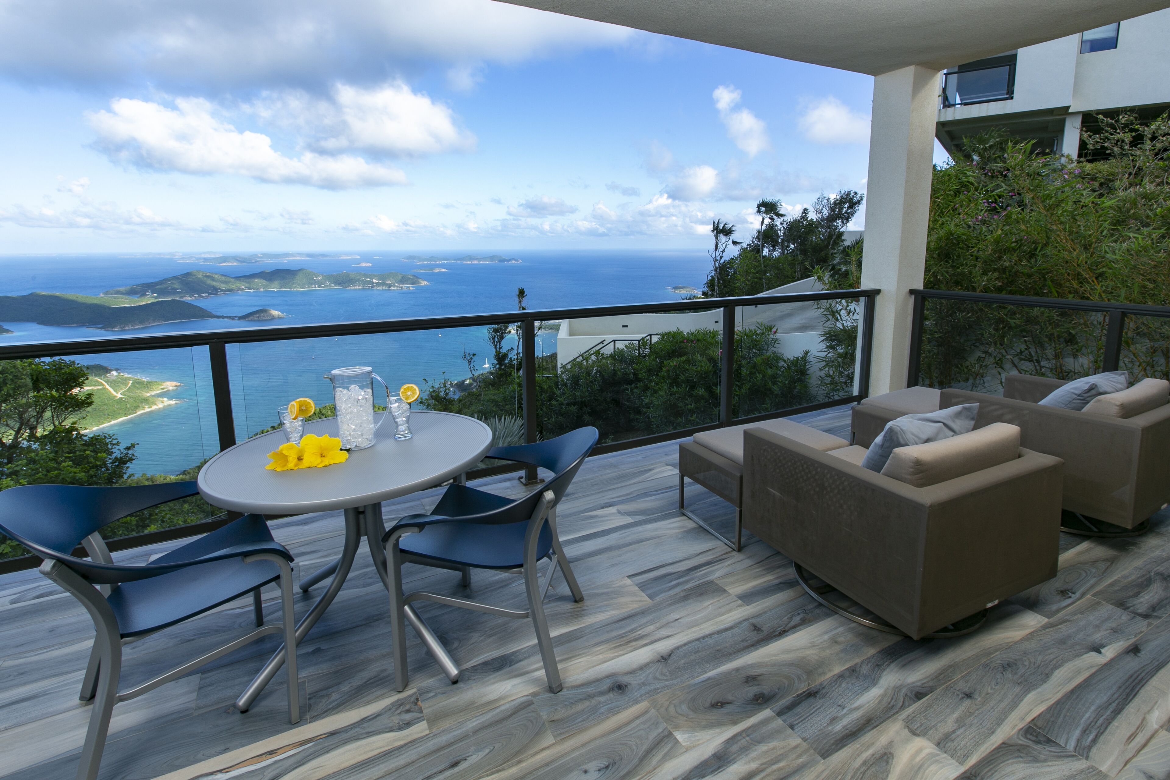 Varanda com mesa, cadeiras, sofá e vista para o mar e colinas.