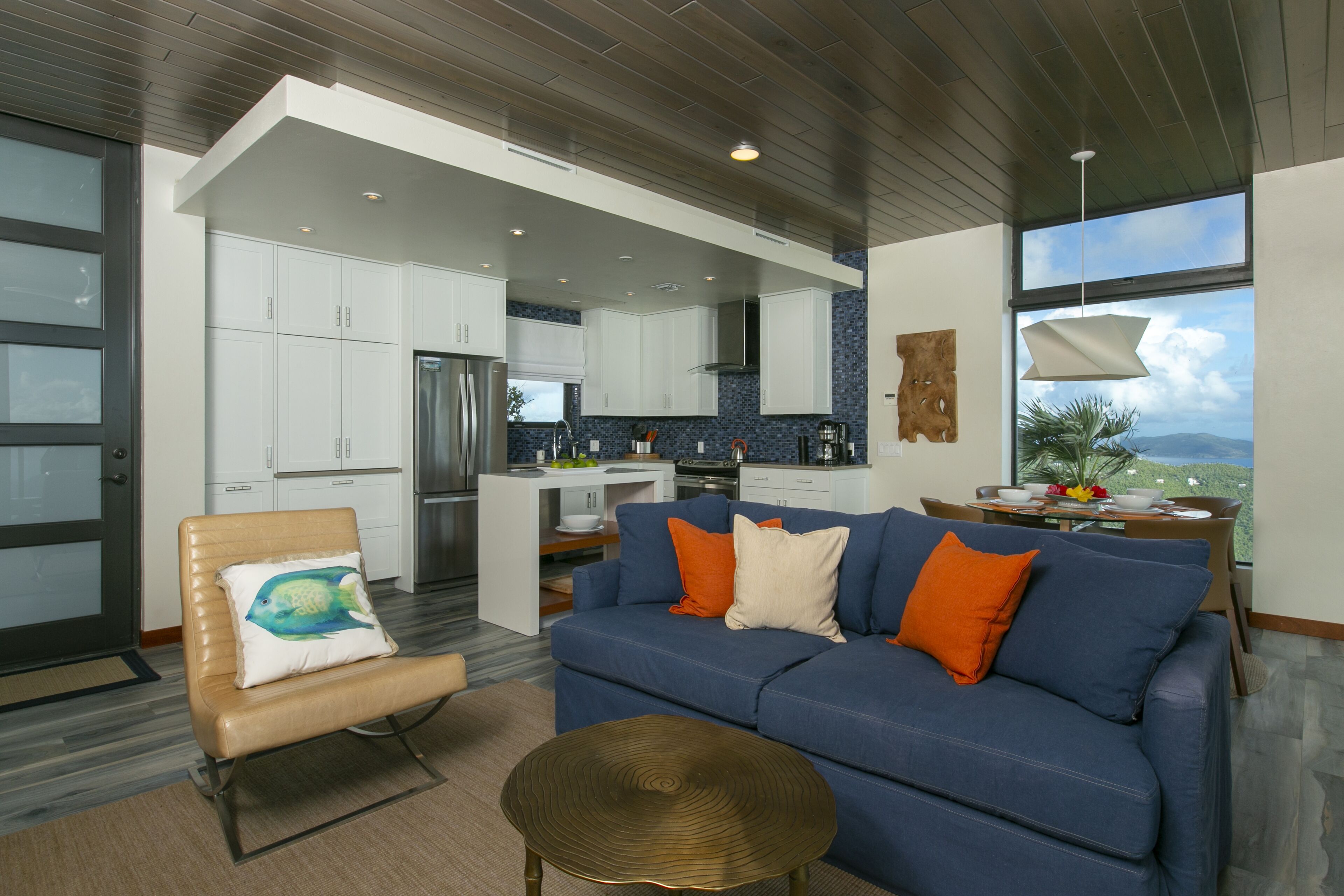 A modern living room with a blue sofa, a wooden chair, and a dining area with a table and chairs.