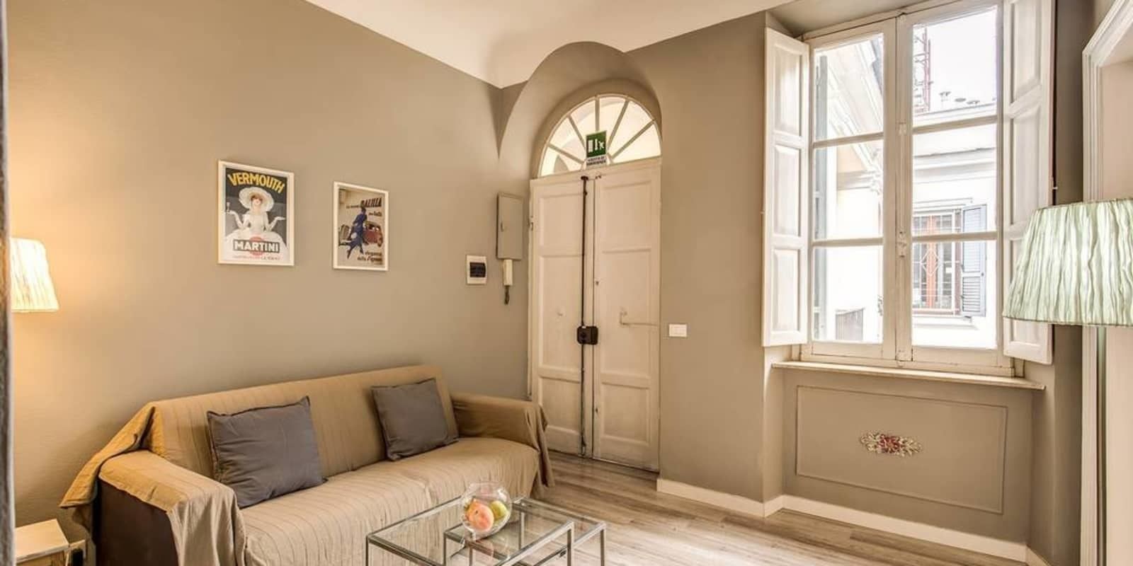 A living room with a beige sofa, a glass coffee table, and two posters on the wall.