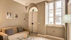 Una sala de estar con un sofá color beige, una mesa de centro de vidrio y dos carteles en la pared.
