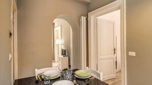 Un comedor con una mesa de mármol, sillas blancas y un espejo que refleja la habitación.