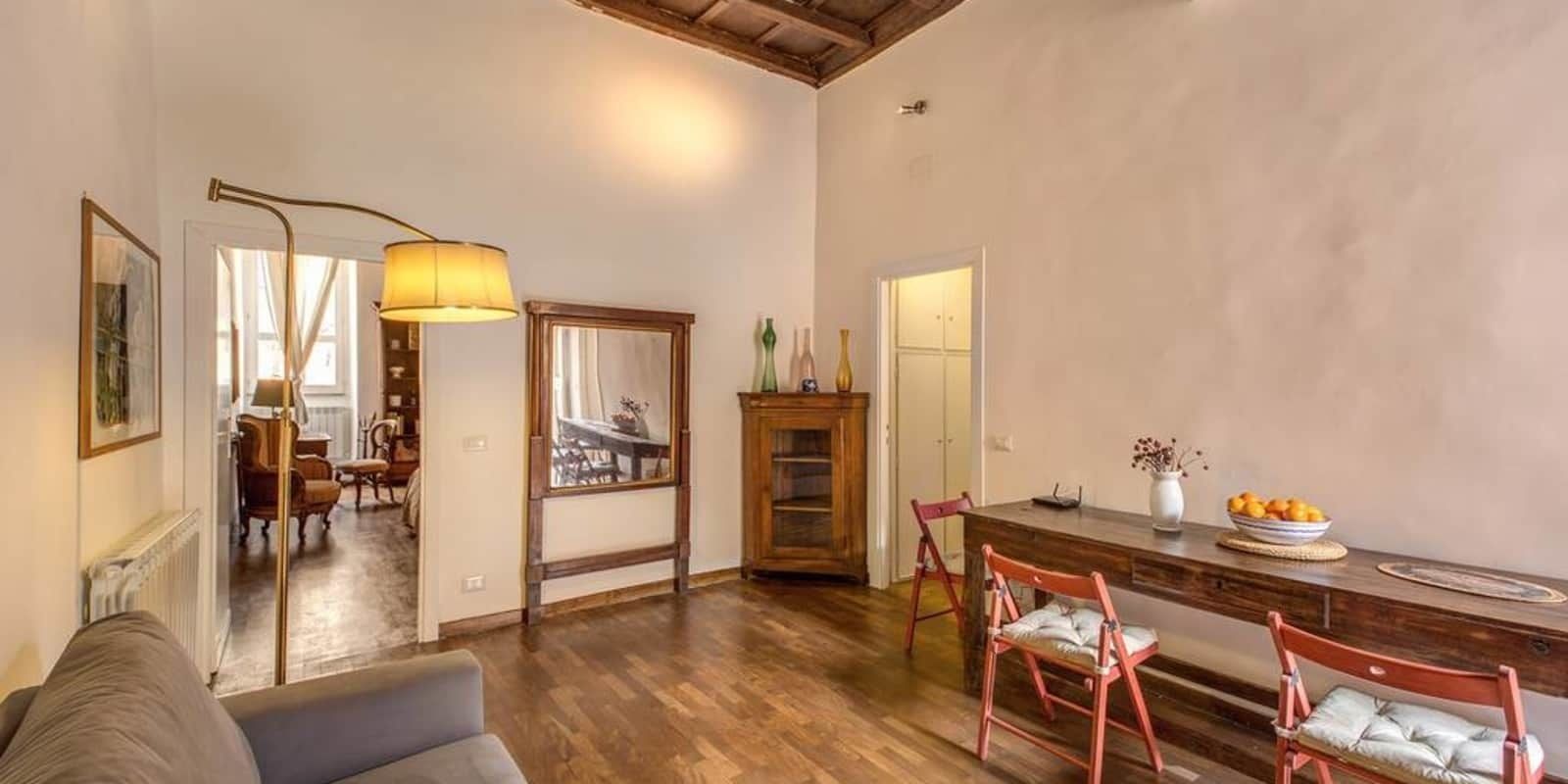 A spacious living room with a wooden floor, a sofa, a dining area with a wooden table and chairs, and a large mirror.